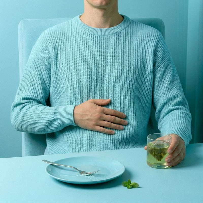 Man in an aqua sweater leaning back after dinner, hand on his stomach, a glass of peppermint tea beside an empty plate